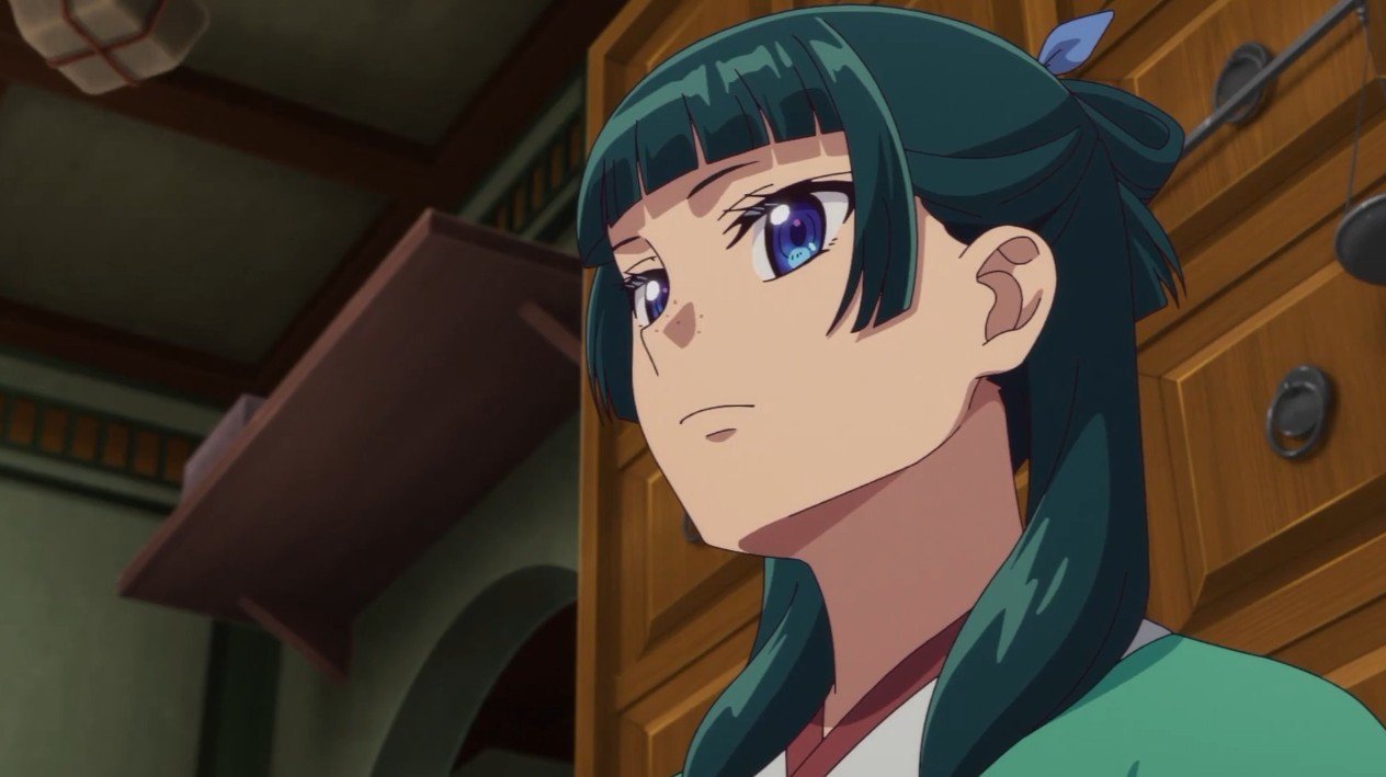 Maomao with dark teal hair and blue-purple eyes looking serious inside a wooden room in The Apothecary Diaries.